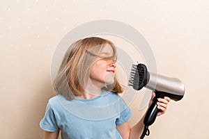 little girl dries her hair with a hair dryer with a comb attachment.