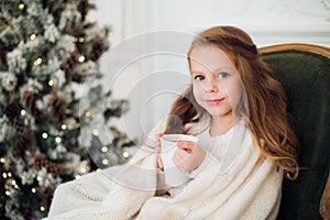 Little girl drinking milk near Christmas tree in morning at home