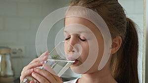 Little girl drinking water from glass in the kitchen at home