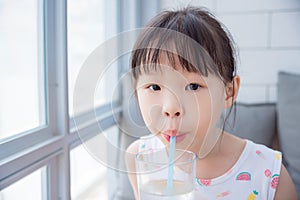 Little girl drinking water from glass via straw