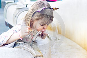 Little girl drinking water on public fountain