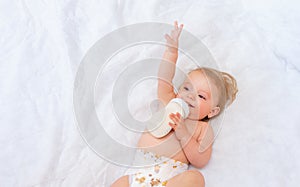 Little girl drinks milk from a bottle while lying on the bed. Baby food. concept of artificial feed