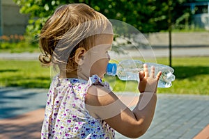 Little girl drinks water from a bottle. Side view.