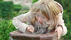 a little girl drinks water from a drinking fountain outside.