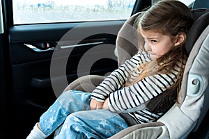 Little girl is driving in car. Kid child wants to go to toilet, pee and endures. Traveling, riding on road in safe baby seats with