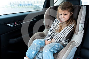 Little girl is driving in car. Kid child wants to go to toilet, pee and endures. Traveling, riding on road in safe baby seats with