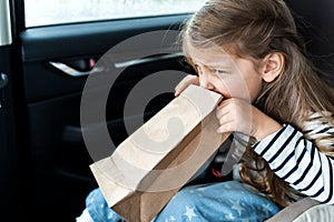 Little girl is driving in car. Kid is sick, feels bad and vomiting into paper bag. Traveling, riding on road in safe baby seats