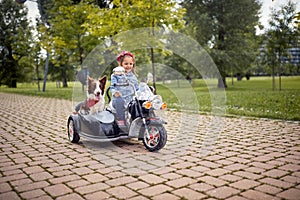 Little girl driving electrical motorcycle toy with a sidecar with a dog in it