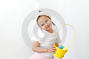 a little girl in an Easter bunny costume holds a basket of colored eggs