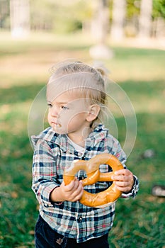 Little girl is eating a big bagel, holding it with both hands and turning her head to the side