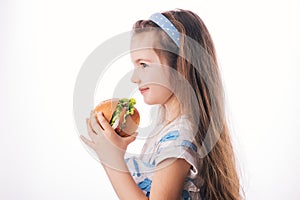 Little girl eating big burger. Kid looking at healthy big sandwich, studio isolated on white background