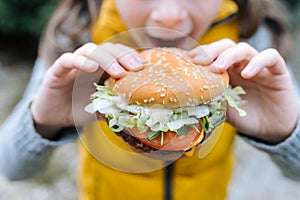 Little girl eating a big cheeseburger with tomato, lettuce, arugula, beef and sauce