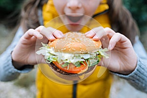 Little girl eating a big cheeseburger with tomato, lettuce, arugula, beef and sauce