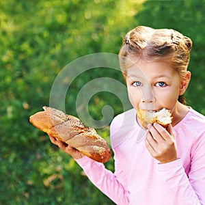 Little girl eating bread. Outdoors female portrait. Look at camera