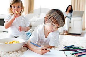 Little girl eating chips and her brother drawing