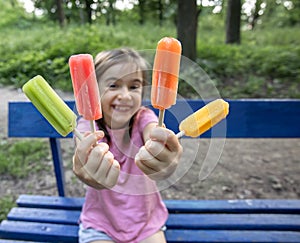 Little girl eating colorful ice cream sitting on a bench