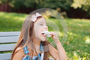 Little girl eating cotton candy sitting on a bench in the park summer