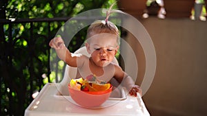 Little girl eating fruit from a bowl while sitting on a high chair on the terrace