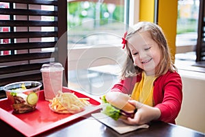 Little girl eating a hamburger in fast food restaurant
