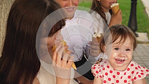 Little girl is eating ice cream sitting on bench in park with her family.