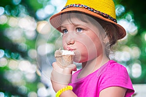 Little girl eating ice cream on the street. Portrait of a babe in a hat with a dessert.