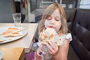 Little girl eating pizza with hand in restaurant