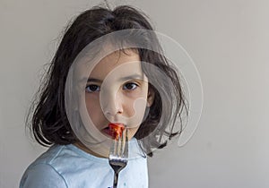 The little girl is eating red tometo with fork