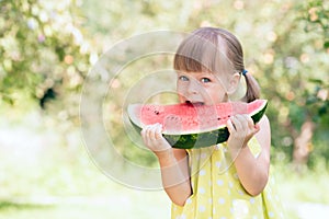 Little girl eating ripe watermelon in sunny summer garden
