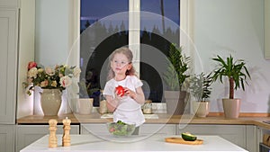 Little girl eating tomato in the kitchen. Happy childhood. Cheerful child eats vegetables and healthy food in the