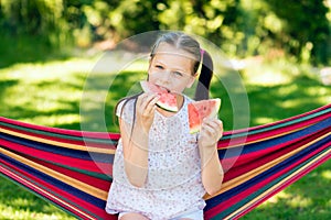 Little girl eating watermelon slices in the garden sitting on a hammock