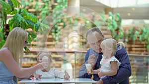The little girl eats ice cream a horn in big shopping center. Family eats ice cream in the mall. Happy family. Cute