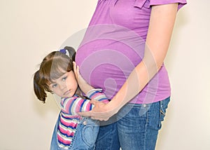 The little girl embraces hands a stomach of pregnant mother