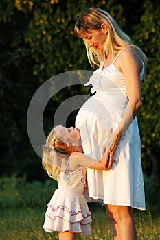 The little girl embraces a pregnant mum