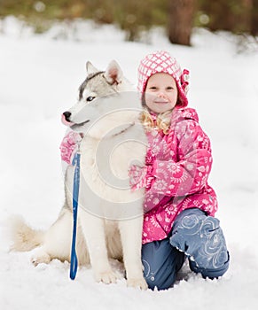 Little girl embracing hasky dog in winter park