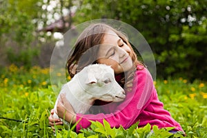 Little Girl Embracing Little Goat In Garden.