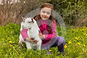 Little Girl Embracing Little Goat On Grass In Garden.
