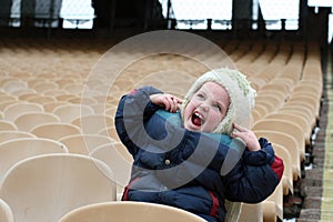 A little girl is on empty zone for fans in the stadium and makes grimaces