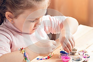 A little girl is engaged in needlework, making jewelry with her own hands, stringing multi-colored beads on a thread