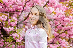 Little girl enjoy spring. Kid on pink flowers of sakura tree background. Kid enjoying cherry blossom sakura. Happy