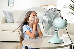 Little girl enjoying air flow from fan. Summer heat