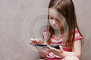 Little girl enthusiastically controls the phone. online learning games