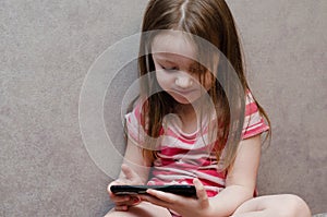 Little girl enthusiastically controls the phone. online learning games