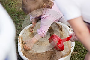 A little girl enthusiastically plays with mud in a basin