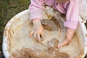 A little girl enthusiastically plays with mud in a basin