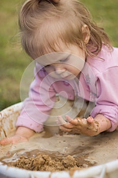 A little girl enthusiastically plays with mud in a basin