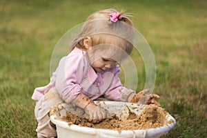 A little girl enthusiastically plays with mud in a basin