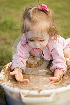 A little girl enthusiastically plays with mud in a basin