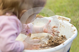 A little girl enthusiastically plays with mud in a basin