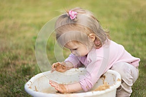 A little girl enthusiastically plays with mud in a basin