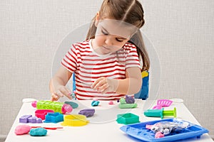Little girl enthusiastically plays with plasticine, play dough on white table at home, children`s creativity